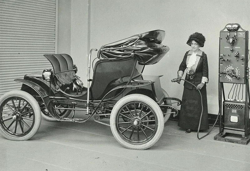 Mujer de época cargando un automóvil eléctrico antiguo en una estación de carga